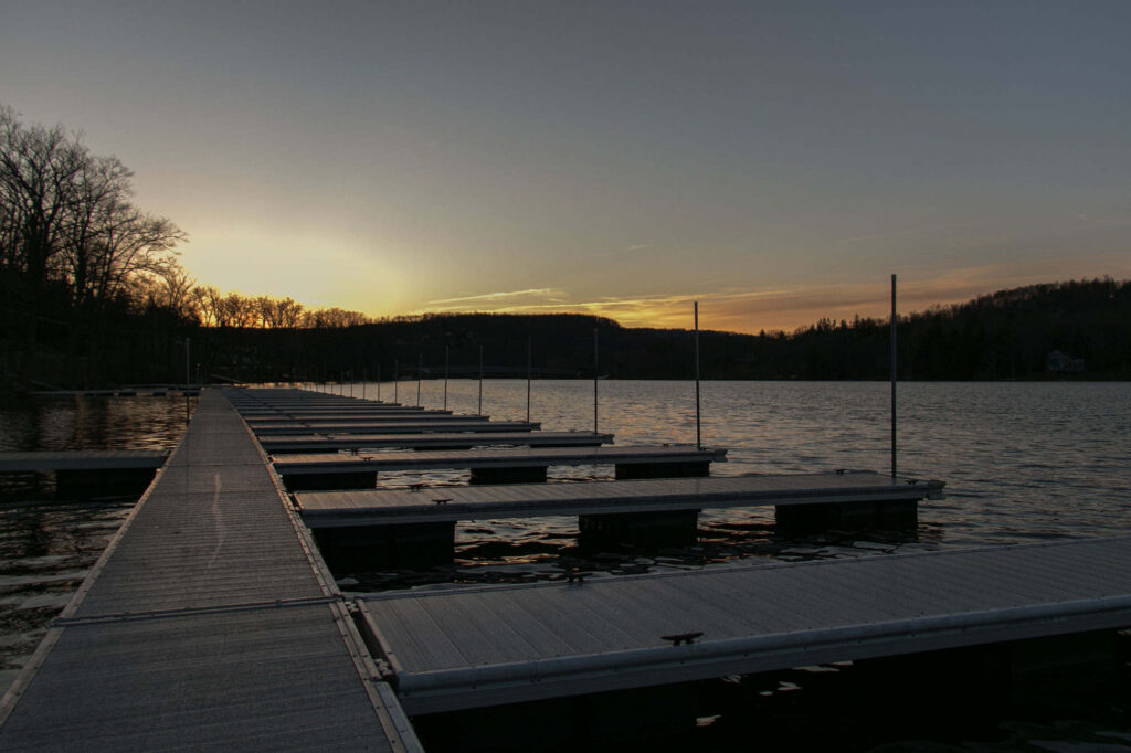Empty docks on a lake at sunset with calm water and silhouetted trees in the background.