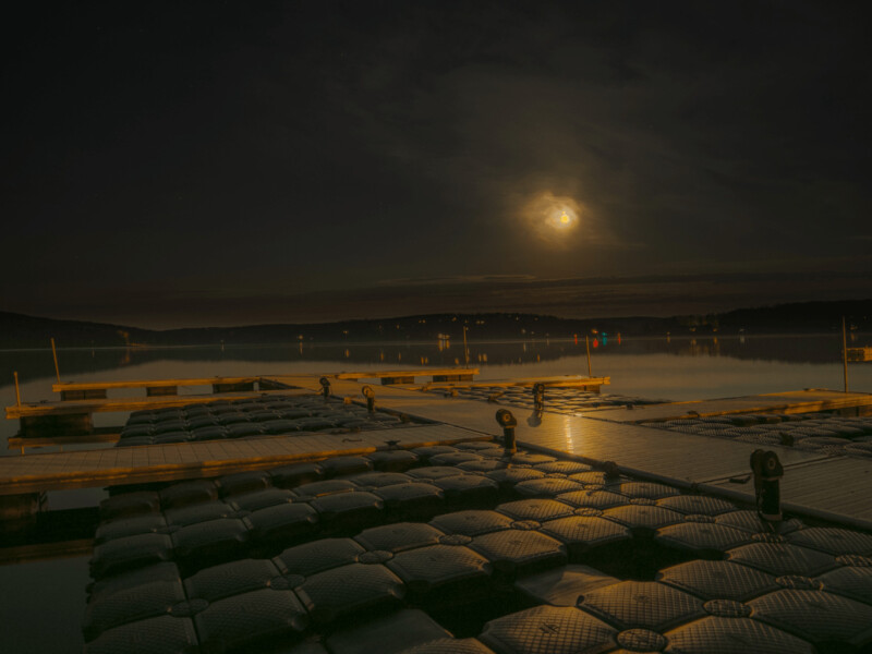 Floating docks on a calm lake at night with the moon shining brightly and reflected on the water's surface.
